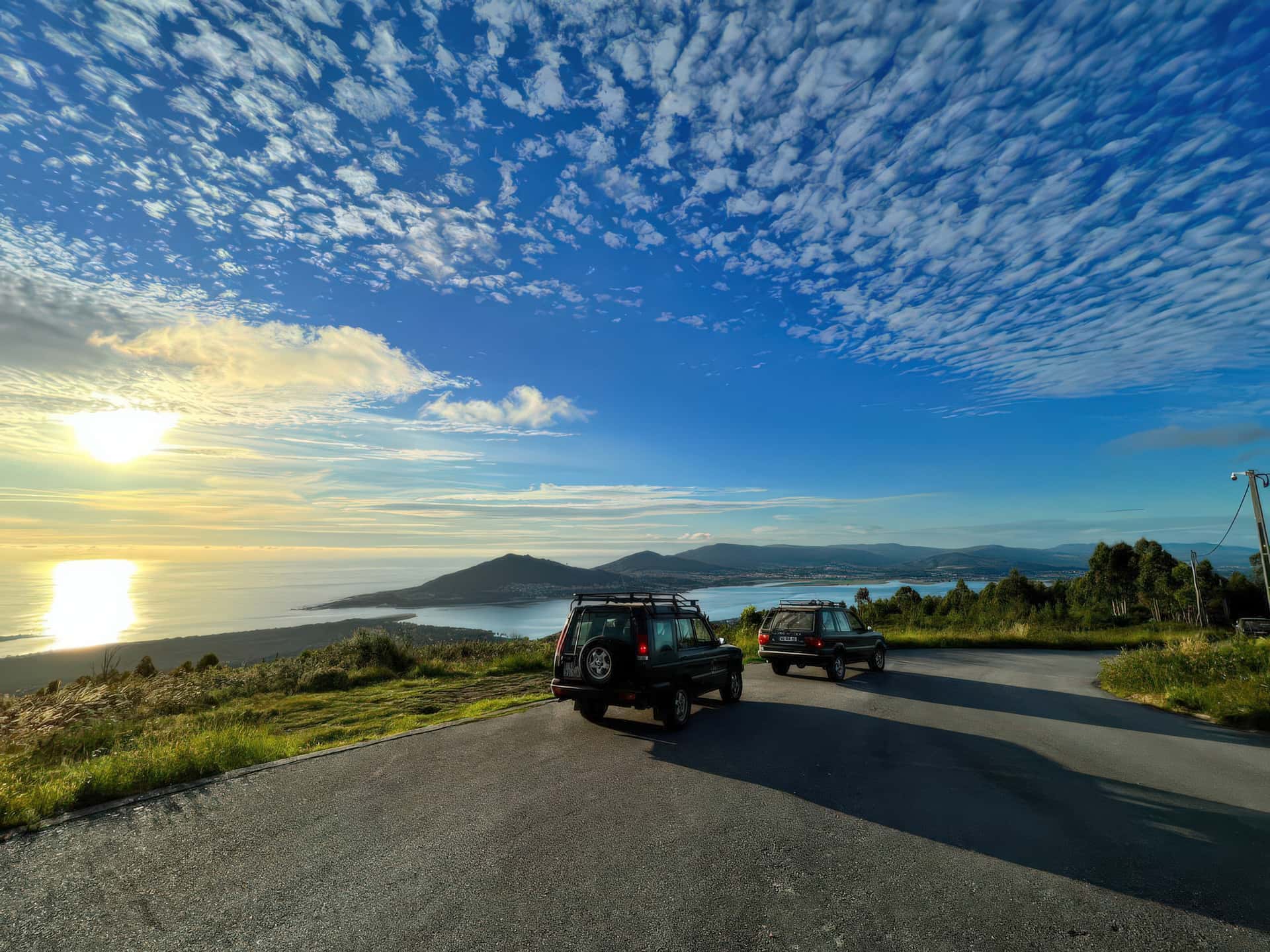 Two four-wheel drives at a clifftop viewpoint above the Portuguese coast at sunset